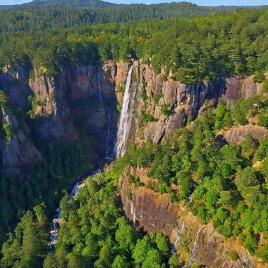 A full shot bird's-eye view of a dramatic mountain cliffside, with deep focus on the sheer drop and the landscape below. The photo captures the vertiginous height of the cliff, with tiny trees and rivers far below adding scale to the image. clipart