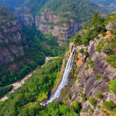 A full shot bird's-eye view of a dramatic mountain cliffside, with deep focus on the sheer drop and the landscape below. The photo captures the vertiginous height of the cliff, with tiny trees and rivers far below adding scale to the image. clipart