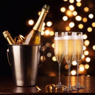 A high-resolution digital artwork features a festive New Year celebration. Central are two glittering champagne flutes filled with golden champagne, alongside an elegant gold ice bucket containing a champagne bottle. The scene is illuminated with clipart