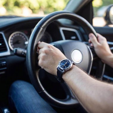 A high-resolution ultrarealistic image capturing a close-up view of a man's hands gripping the steering wheel of a modern car. The photograph highlights the detailed texture of the steering wheel and the man's skin, complemented by a sleek watch on clipart