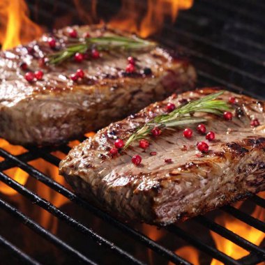 A high-resolution photo capturing two thick, juicy steaks sizzling on a black grill grate. The steaks' surfaces are seared to perfection, with a glistening, caramelized crust and adorned with fresh sprigs of rosemary. Red and black peppercorns dot clipart