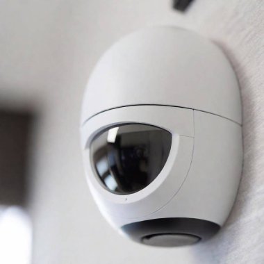 A high-resolution ultrarealistic image showcasing modern surveillance and smart home technology. The image captures a close-up of a sleek, white dome security camera mounted on a white ceiling, showcasing its polished, semi-transparent black dome clipart