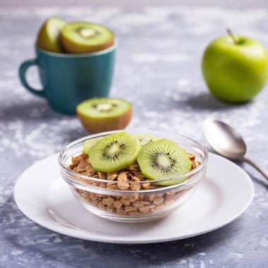 A high-resolution ultrarealistic image of a breakfast scene. The central focus is a clear glass bowl filled with granola and milk, topped with fresh kiwi and banana slices. The bowl is placed on a white plate with a white spoon. To the left, there clipart