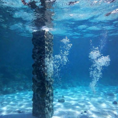 A high-resolution ultrarealistic image captures the underwater scene in photographic style. The frame shows a column of air bubbles rising through clear, dark blue water, with the light gently illuminating their forms. The bubbles, varying in size clipart