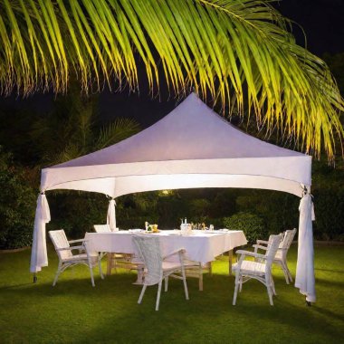 A high-resolution photograph capturing a nighttime scene of a warmly lit makeshift tent adorned with colorful decorations and resembling a traditional outdoor dining spot. The structure, made with white sheets and covered by a roof of palm leaves clipart