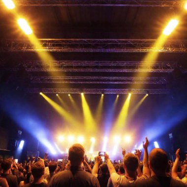 A high-resolution ultrarealistic image captures a vibrant concert scene with a dynamic atmosphere. The digital photograph shows a crowd with raised hands, immersed in the music. Concert lighting fixtures cast warm, golden hues over the scene clipart