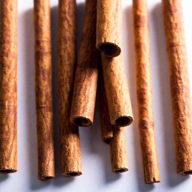 A high-resolution photograph showcases five cinnamon sticks arranged in a casual pile against a pristine white background. The image captures the intricate textures and warm, rich brown hues of the cinnamon bark, with the characteristic rolled edges clipart