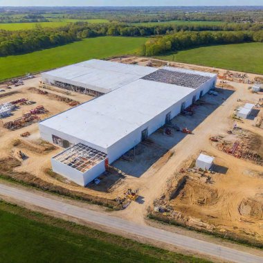 An aerial photo of a warehouse construction project, capturing the scale of the building site with various stages of construction, including the framework, materials, and equipment spread across the area clipart