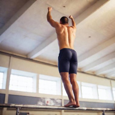 Rear view of a young adult male gymnast performing a high bar routine, captured with deep focus from a low angle, highlighting his form and the entire gym environment in the background clipart