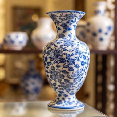 porcelain vase with intricate blue and white patterns, at eye level with rack focus shifting from the delicate floral design in the foreground to a blurred background of other porcelain pieces in a display case. clipart