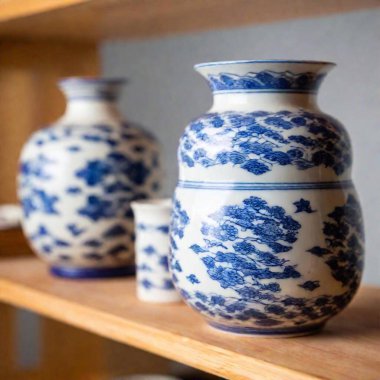 Eye-level medium shot of a display of Ming Dynasty-style porcelain, with rack focus shifting from a detailed close-up of a single piece to a soft blur of the surrounding collection of similar vases and plates. clipart