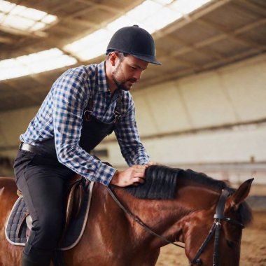 A medium close-up of a jockey's expression of concentration as they prepare to mount their saddled horse. clipart