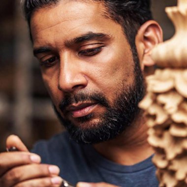 A macro shot of a Latino artisan carefully carving a wooden sculpture in his workshop. The extreme close-up captures the intricate details of the carving tools and wood shavings around him. clipart