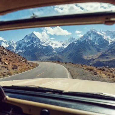 A nostalgic, grainy view of snow-capped mountains through a dusty windshield, the vintage car dashboard visible, with scratches adding a timeless, analog feel to the image. clipart