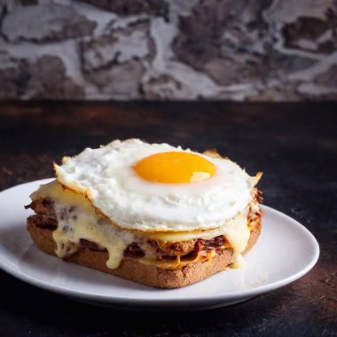 Close-up of a croque madame served on a simple white plate, the dark background highlighting the crispy edges and layers of ham, cheese, and bechamel sauce. clipart