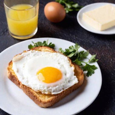 A croque madame on a minimalist white plate, set against a dark background, with close-up focus on the golden, bubbly cheese and the egg slightly dripping yolk. clipart