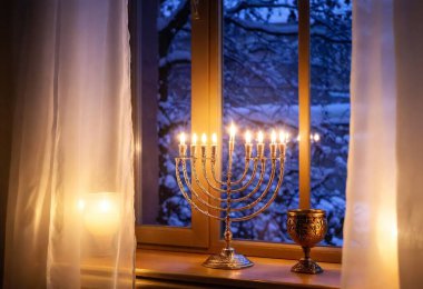 A wide shot of a winter evening window with Hanukkah lights shining from the interior, with a softly illuminated menorah visible through the glass. clipart