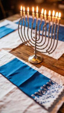 A low-angle view of a decorated wooden tabletop featuring a metal menorah surrounded by colorful Hanukkah gelt and delicate blue napkins. clipart