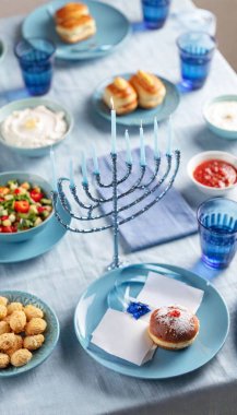 A full shot of a blue-themed Hanukkah dinner setting with a menorah in the middle, surrounded by bowls of food and festive blue plates. clipart