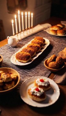 A medium-wide shot of a festive dinner table with a glowing menorah in the middle, next to decorative bowls of latkes, gefilte fish, and challah bread. clipart