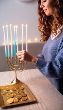 A side view of a female arranging a Hanukkah centerpiece, placing gelt coins near the menorah's light with small blue candles glowing softly. clipart