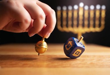 A close-up shot of a female's hand spinning a dreidel on a wooden surface, with a lit menorah in the background. clipart