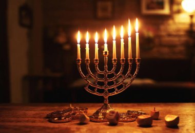 A front view of a single candle of the menorah burning brightly, surrounded by gold gelt, dreidels, and a cozy, dimly lit room. clipart