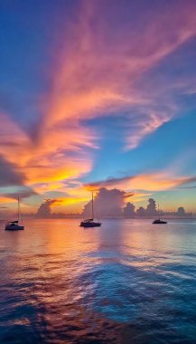 A surreal sunset with skies painted in neon pinks, electric blues, and fiery oranges reflecting off crystal-clear turquoise waters, dotted with distant silhouettes of sailboats. clipart