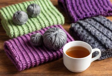 Hand-knit Winter Accessories: A selection of soft, hand-knitted scarves, mittens, and hats in vibrant patterns, displayed with yarn, knitting needles, and a steaming cup of tea beside them clipart