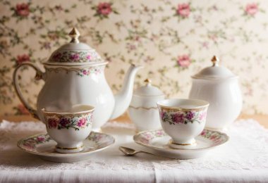 Porcelain Tea Set: A delicate antique tea set with floral patterns in soft pastel hues, arranged with a matching sugar bowl, silver spoons, and lace napkins on an embroidered tablecloth. clipart