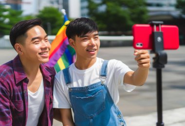 Asian couple taking selfie with mobile phone in city. happy gays clipart