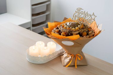 Creative bouquet made of dried fruits and nuts wrapped in kraft paper, decorated with orange ribbon and a 