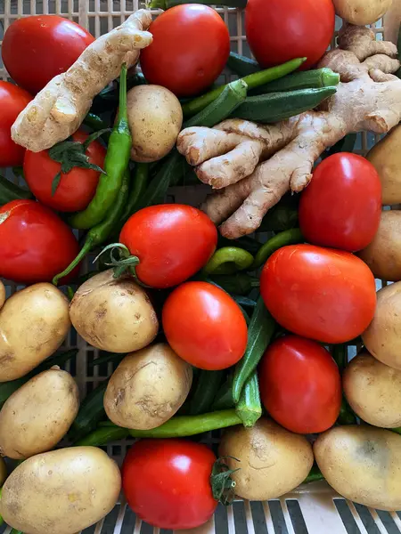 stock image A top-down view showcases a vibrant array of fresh red tomatoes, aromatic ginger, fiery green chilies, and earthy potatoes.