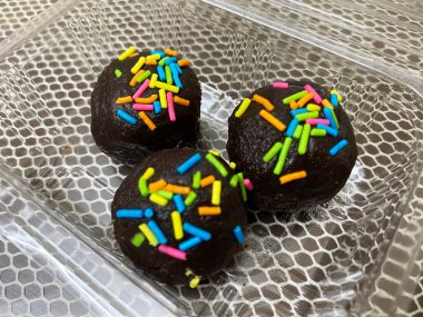 Lezzetli, küresel bir çikolata bombası, parlak, zengin, siyah çikolata yüzeyi davetkar ve yozlaşmış. Bomba, neşeli ve şen şakrak bir şekilde serpiştirilmiş renkli bir dizi süsleme ile cömertçe süslenmiş.