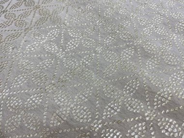 Altın badala işçiliğiyle işlenmiş geometrik bir çiçek deseni bej ipek kumaşta zarifçe parıldıyor..