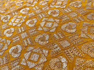 A close-up view of a golden geometric tikki motif on mustard georgette fabric clipart