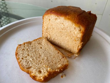 Düzgünce dilimlenmiş vanilyalı sünger keki yumuşak, kabarık katmanlarını ortaya çıkarıyor, kalan tüm pastanın yanında zarifçe oturuyor, mükemmel bir ısırığı davet ediyor..