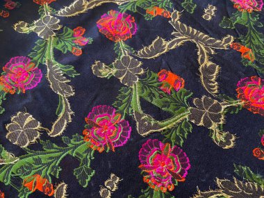 Siyah ipek ipeklerin ters tarafı canlı, renkli dokuma ipliklerinden oluşan bir görüntü sergiliyor. Hassas çiçek desenlerini oluşturan titiz işçiliği gözler önüne seriyor..