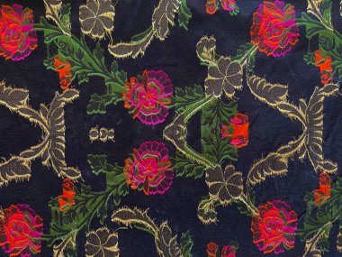 Siyah ipek ipeklerin ters tarafı canlı, renkli dokuma ipliklerinden oluşan bir görüntü sergiliyor. Hassas çiçek desenlerini oluşturan titiz işçiliği gözler önüne seriyor..