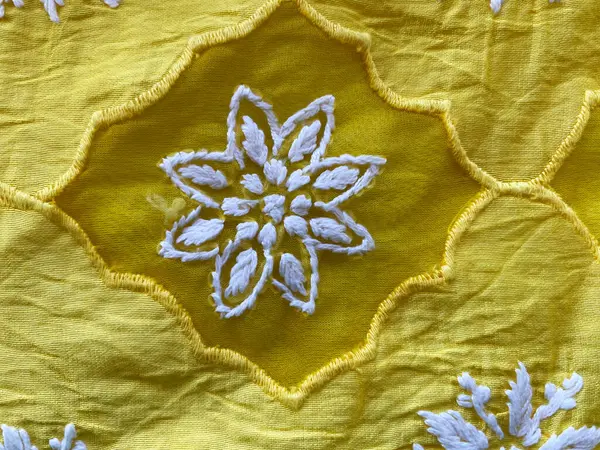 Hassas beyaz iplik işlemeli çiçek butta yama işi bu havadar sarı organza kumaşı süslüyor, zarif ve zarif bir görünüm yaratıyor..