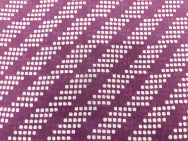 Küçük geometrik noktalı izler, canlı mor pamuk kumaş üzerinde ritmik ve tekrarlayan bir kalıp yaratarak zengin ve cesur arkaplana derinlik ve hareket katıyor..