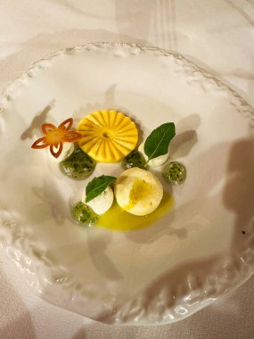 Kalıplı sarı bir meyveyi gösteren sanatsal bir kompozisyon. Yanında da krema ya da köpük, taze fesleğen yaprağı ve şeffaf parlak bir jel var. 