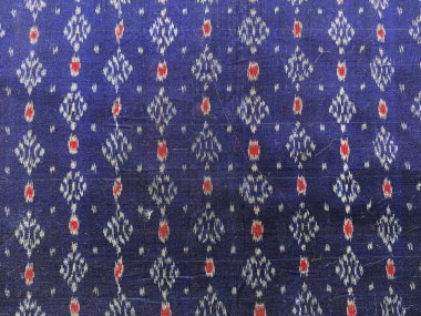 Koyu mavi ipek, yüzeyinde canlı kırmızı ve mavi geometrik desenlerin dans ettiği karmaşık bir Ikat dokumasıyla canlanır..