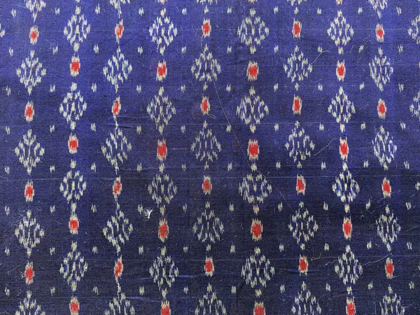 Koyu mavi ipek, yüzeyinde canlı kırmızı ve mavi geometrik desenlerin dans ettiği karmaşık bir Ikat dokumasıyla canlanır..