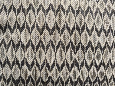 Kumaş, ışık ve karanlık ipliklerin titiz bir şekilde dokumasıyla oluşan cesur bir geometrik desen sergiliyor..