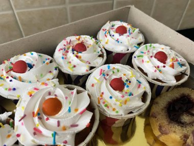 Bir tepsi dolusu altın karamela keki kremalı şekerlemelerle dolu, her biri hoş bir şekilde renkli şekerlemeler ve parlak kırmızı bir kirazla kaplı..