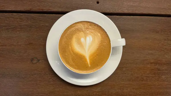 Ahşap masada bir fincan sıcak latte sanatı. en üstteki görünüm.