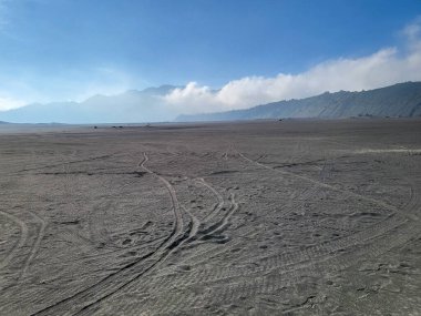 Bir volkanın arka planına karşı bir kum denizi krateri hala aktif olarak volkanik duman yayıyor. Bromo Tengger Semeru Ulusal Parkı, Doğu Java, Endonezya.