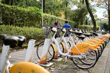 Tayvan - 29 Ocak 2024: Bir çift, Daan Ormanı Parkı yakınlarındaki Youbike istasyonundan geçiyor. Tayvan 'da kısa seyahatler için popüler bisiklet paylaşım sistemi.