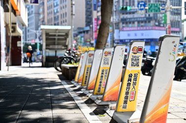 Taiwan - Jan 29, 2024: Empty shared bicycle dock at MRT Dongmen Station during rush hour with cyclist in background. clipart